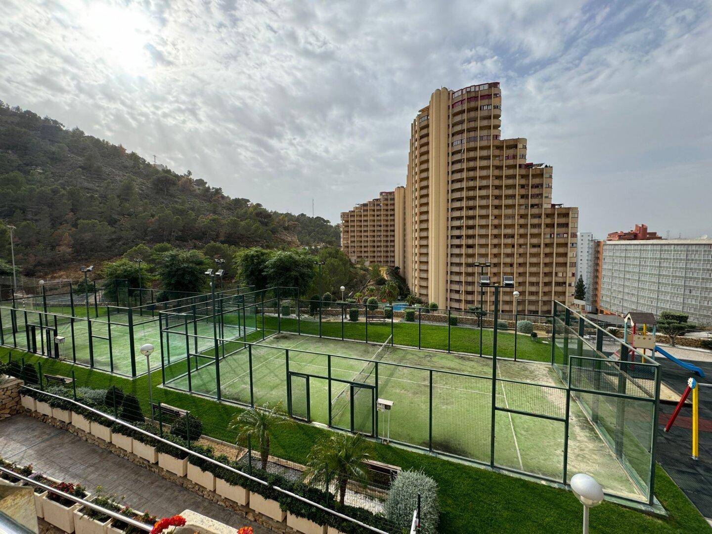 Umfassende Sportanlagen mit Padel-Tennisplätzen und einem Kinderspielplatz, umgeben von Wohngebäuden.