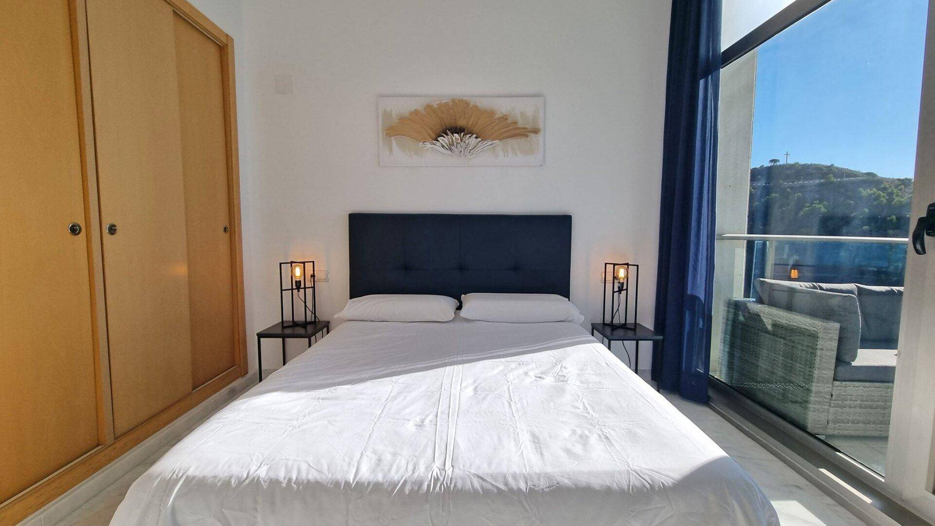 Schlafzimmer mit integriertem Kleiderschrank und großen Fenstern, die viel Tageslicht hereinlassen.