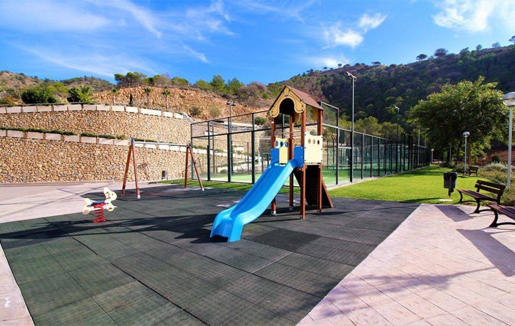 Bunter Kinderspielplatz mit Rutsche und Schaukeln, angrenzend an die Sportanlagen der Wohnanlage.