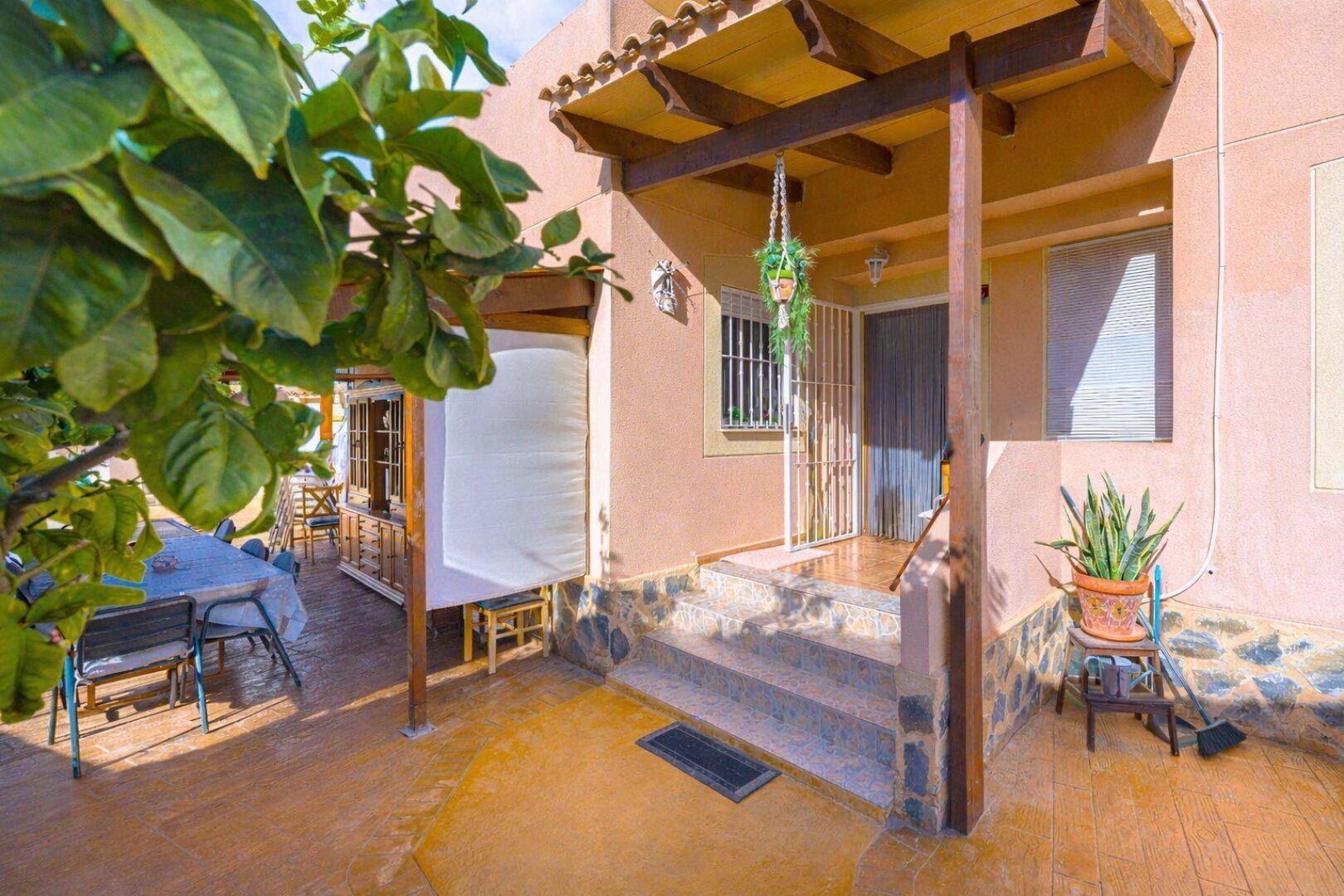 Überdachte Terrasse mit Esstisch unter einem Baum, ideal für Mahlzeiten im Freien.