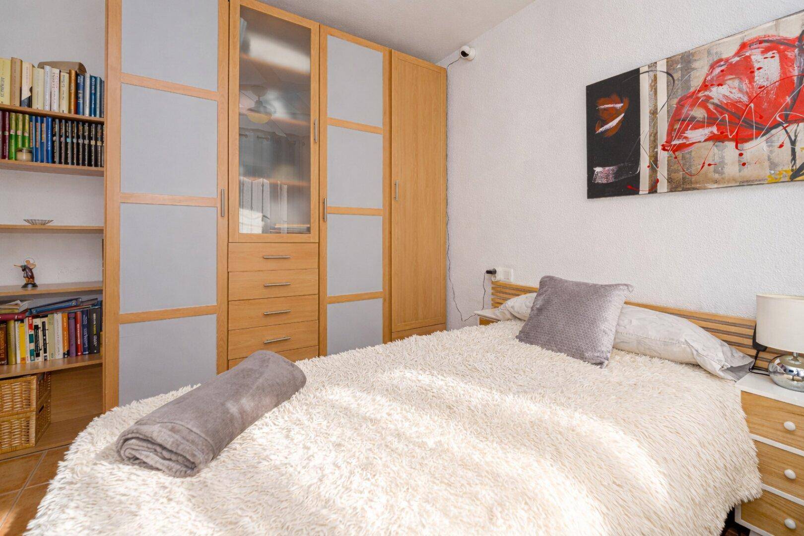 Schlafzimmer mit Terrakottafliesen, Einbauschränken und Bücherregal, gemütlich eingerichtet.