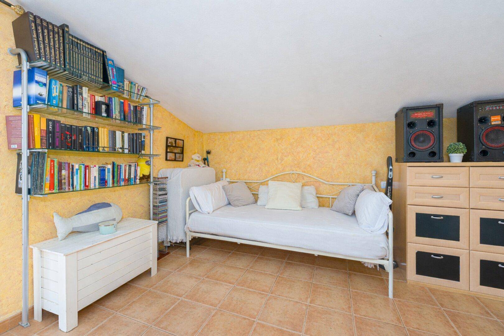 Dachzimmer mit gelben Wänden, Schlafsofa und Bücherregal, vielseitig nutzbar.