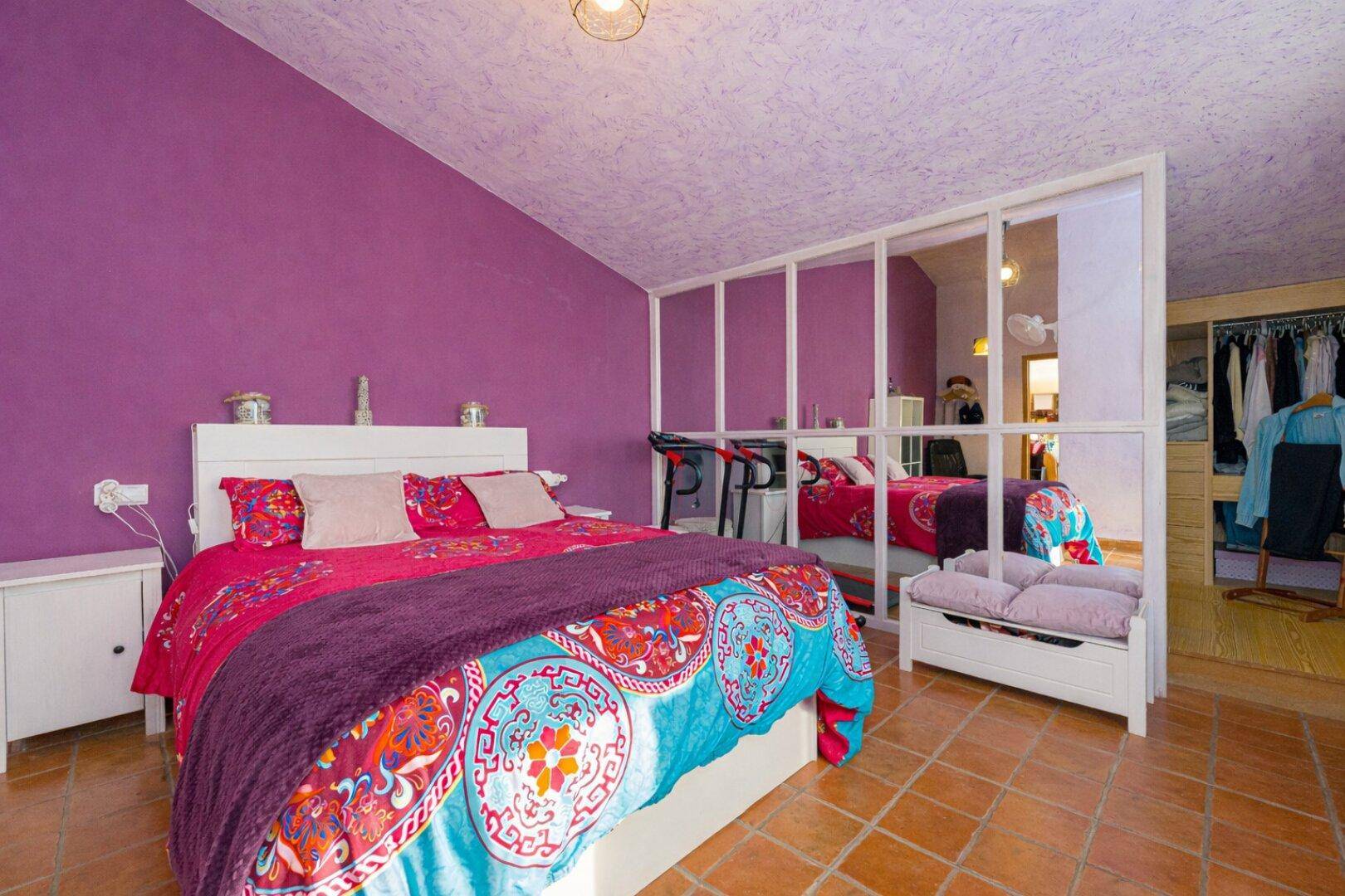 Dachgeschoss-Schlafzimmer mit lila Wänden, Terrakottafliesen und Raumteiler.