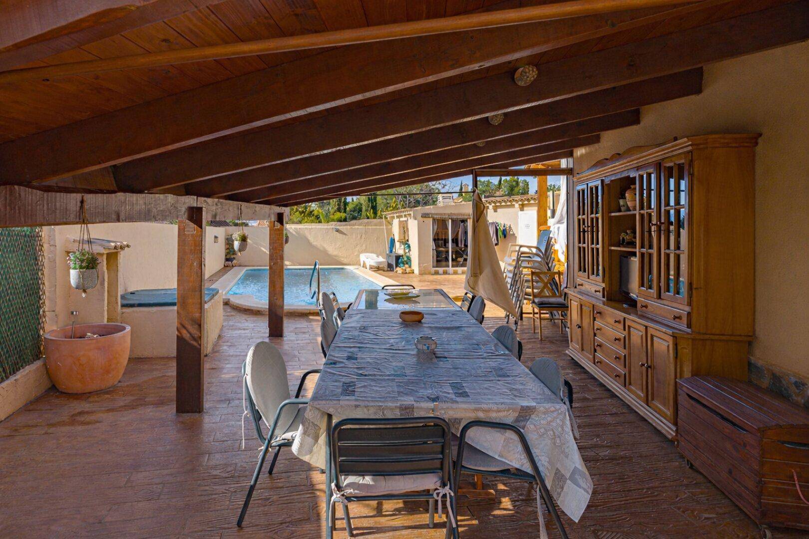 Große überdachte Terrasse mit Esstisch und Blick auf den Poolbereich.