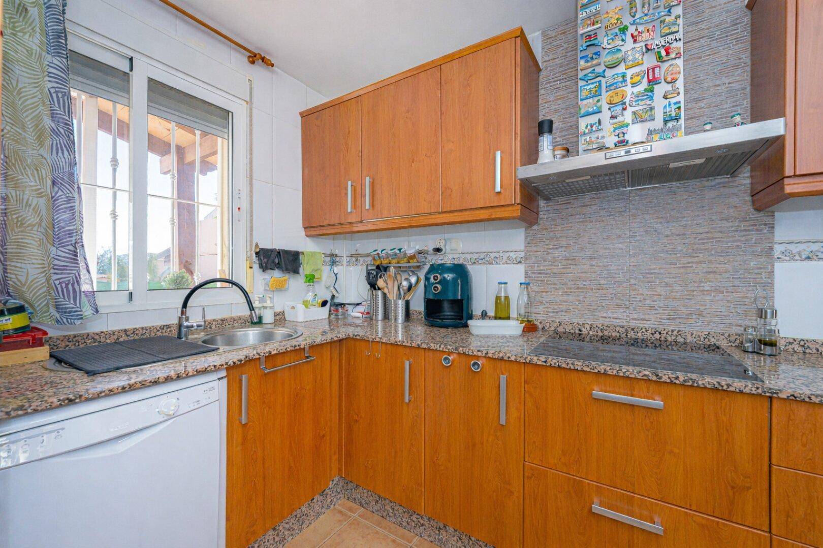Helle Küche mit Fenster, Holzschränken, Granitarbeitsplatten und Spülmaschine.