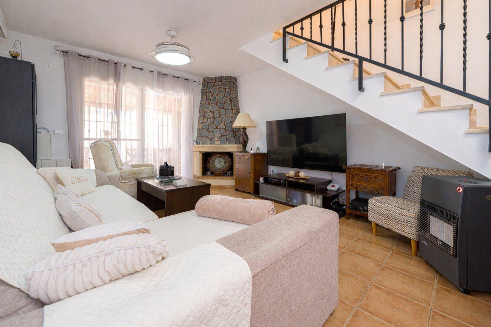 Helles Wohnzimmer mit Treppe zum Obergeschoss, Kamin und großem Fernseher.