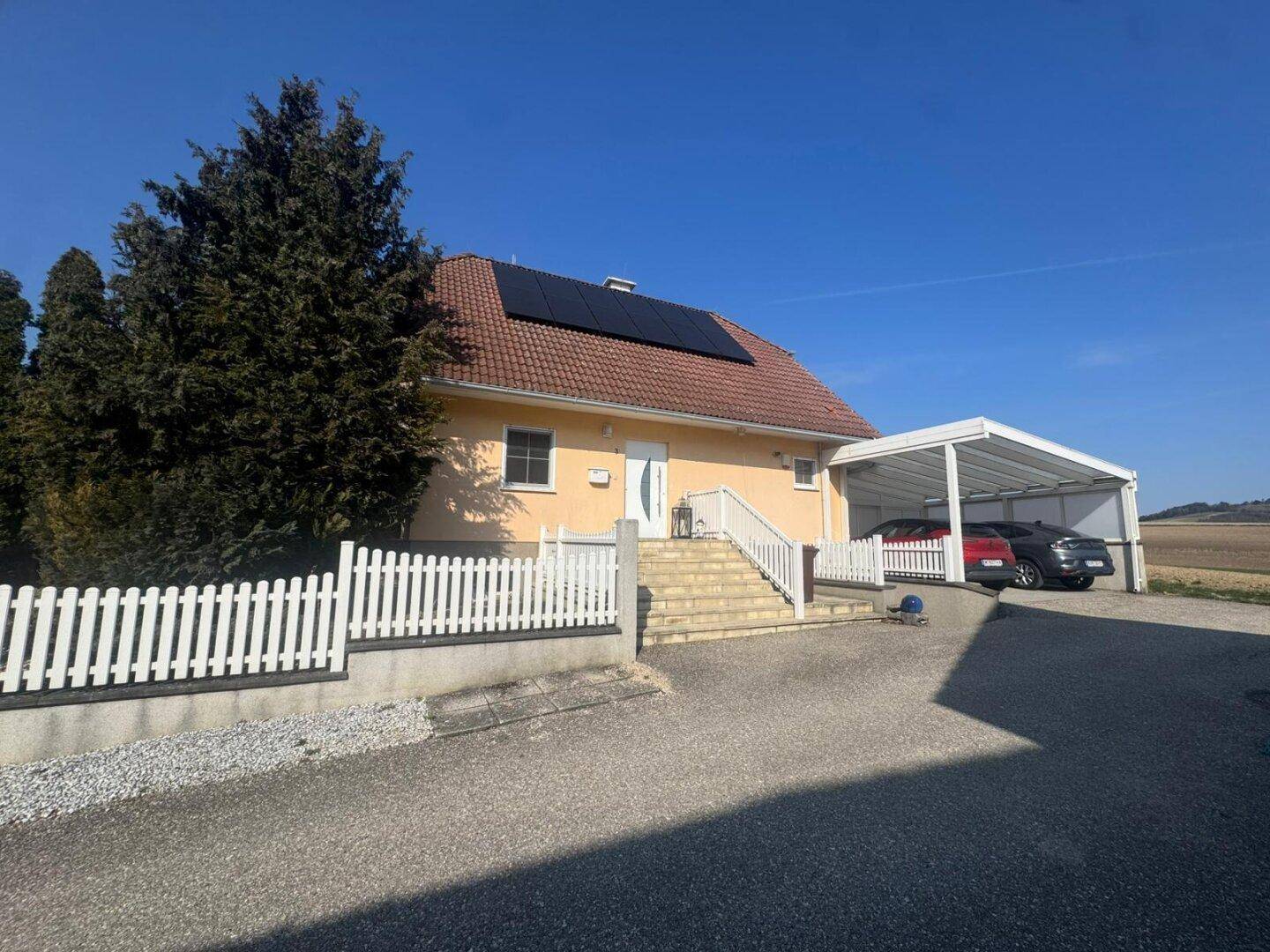 Vorderansicht des Hauses mit Carport für zwei Fahrzeuge und Photovoltaikanlage auf dem Dach.