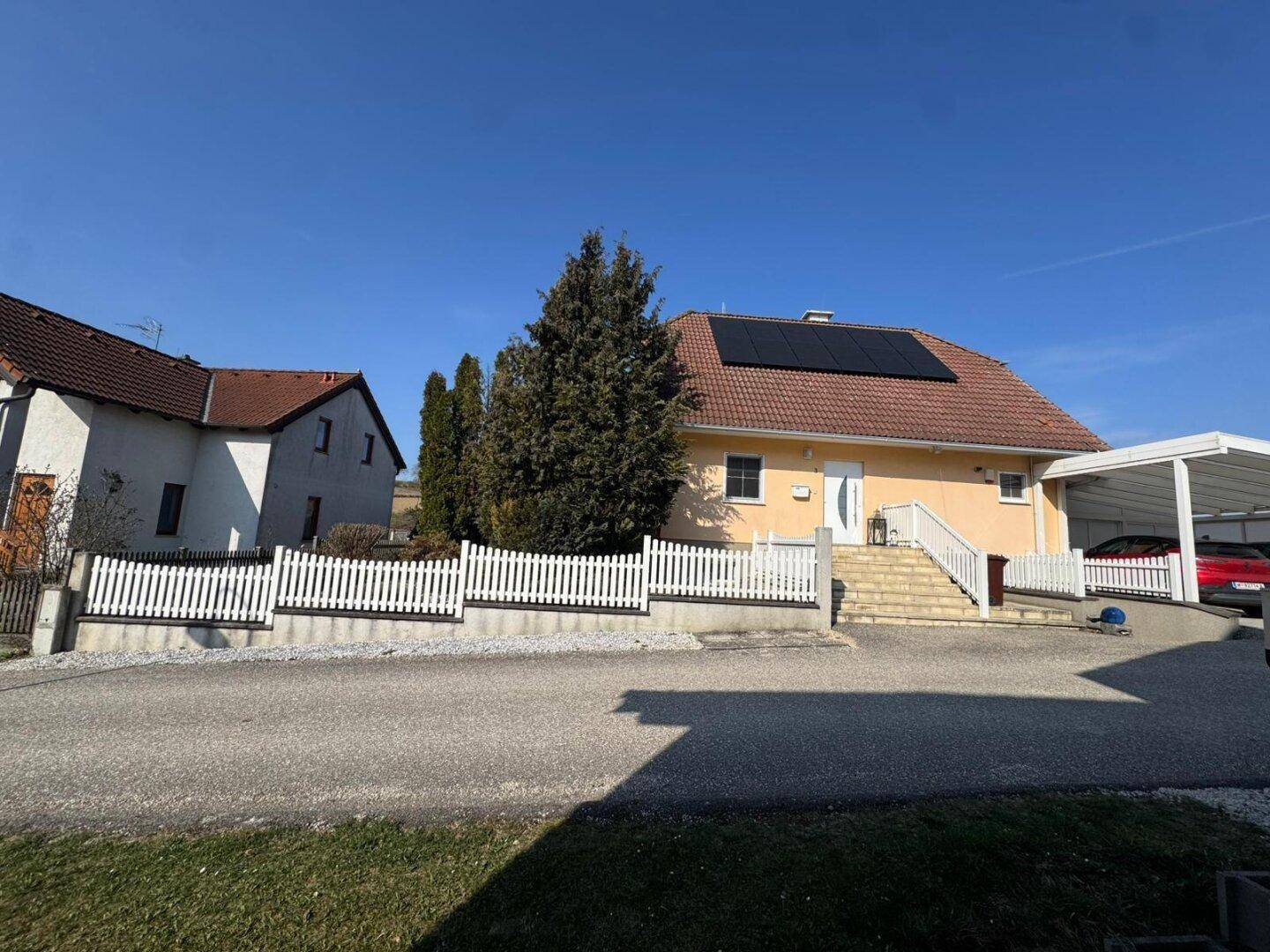 Das Einfamilienhaus mit Photovoltaikanlage und Carport, umgeben von ländlicher Bebauung.