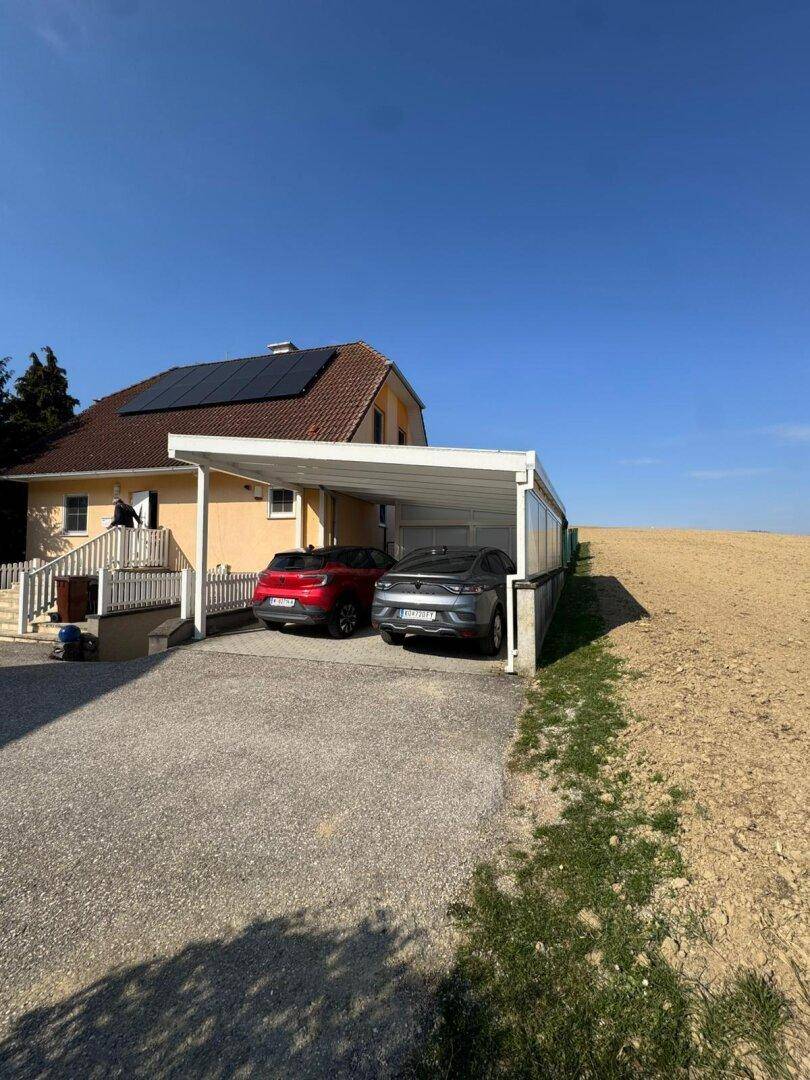 Carport mit zwei Fahrzeugen neben dem Haus, direkt angrenzend an ein weites Feld.
