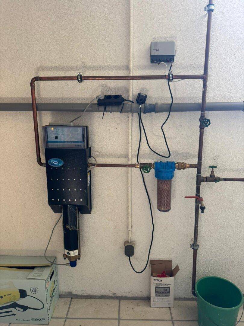 Technischer Raum mit Wasserleitungen und einem Filtersystem an der Wand.