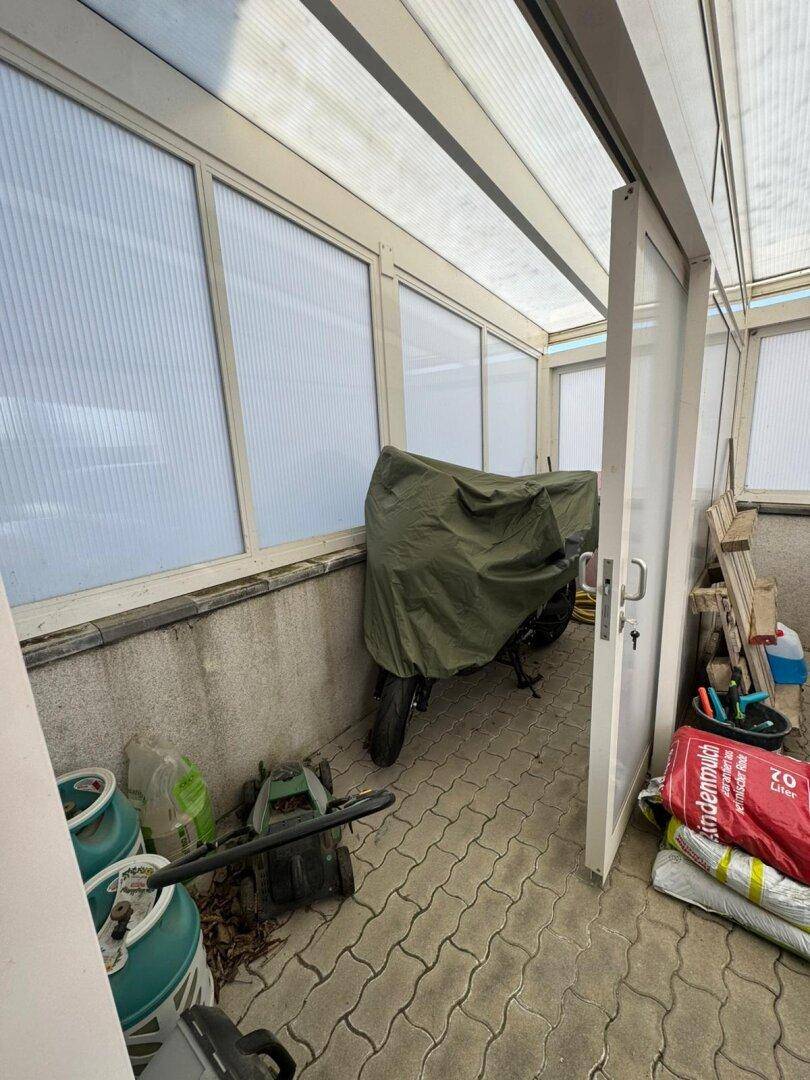 Überdachter Wintergarten oder Anbau mit gepflastertem Boden und einem abgestellten Motorrad.