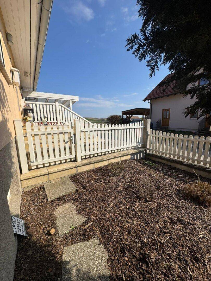 Kleiner Gartenbereich mit Rindenmulch und einem weißen Lattenzaun.