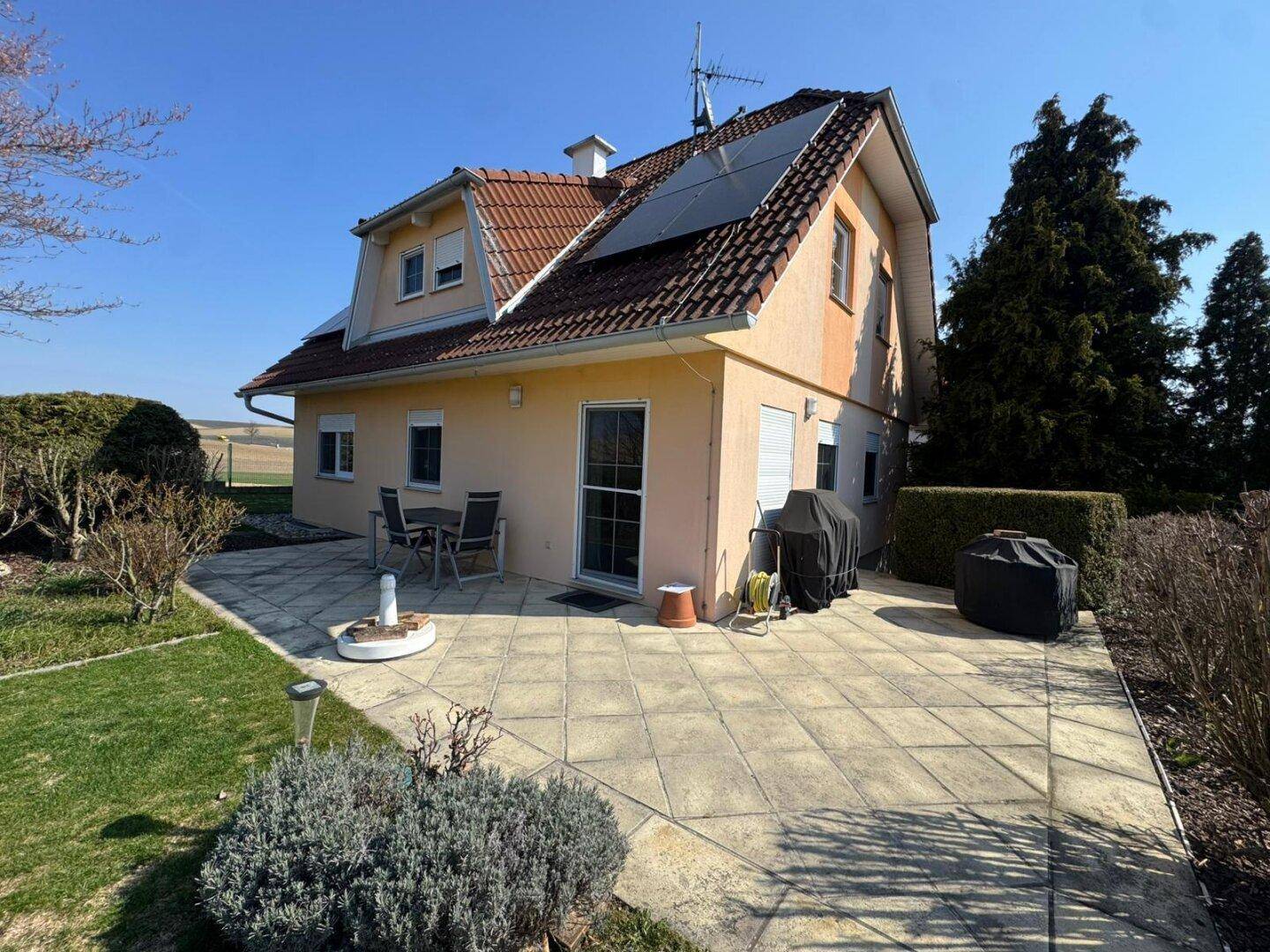 Große gepflasterte Terrasse hinter dem Haus mit Gartenmöbeln und Grillbereich.