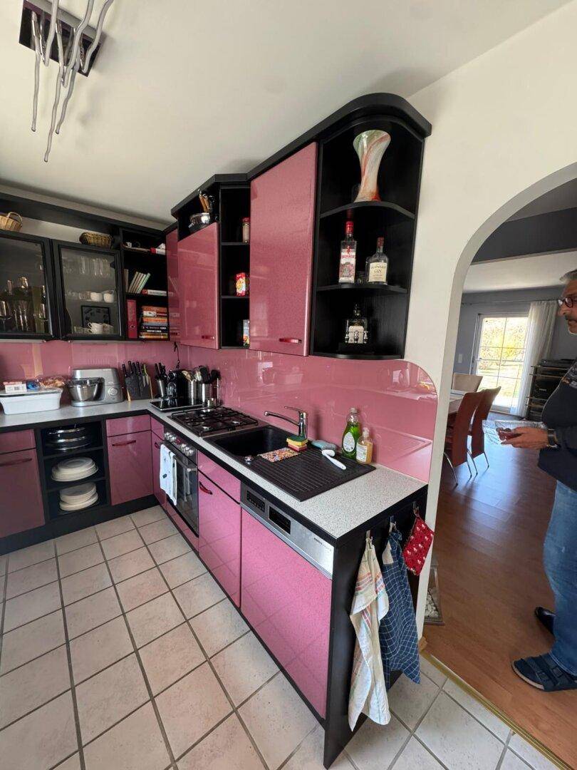 Pinkfarbene Küche mit Spüle, Kochfeld und offenem Durchgang zum Essbereich.