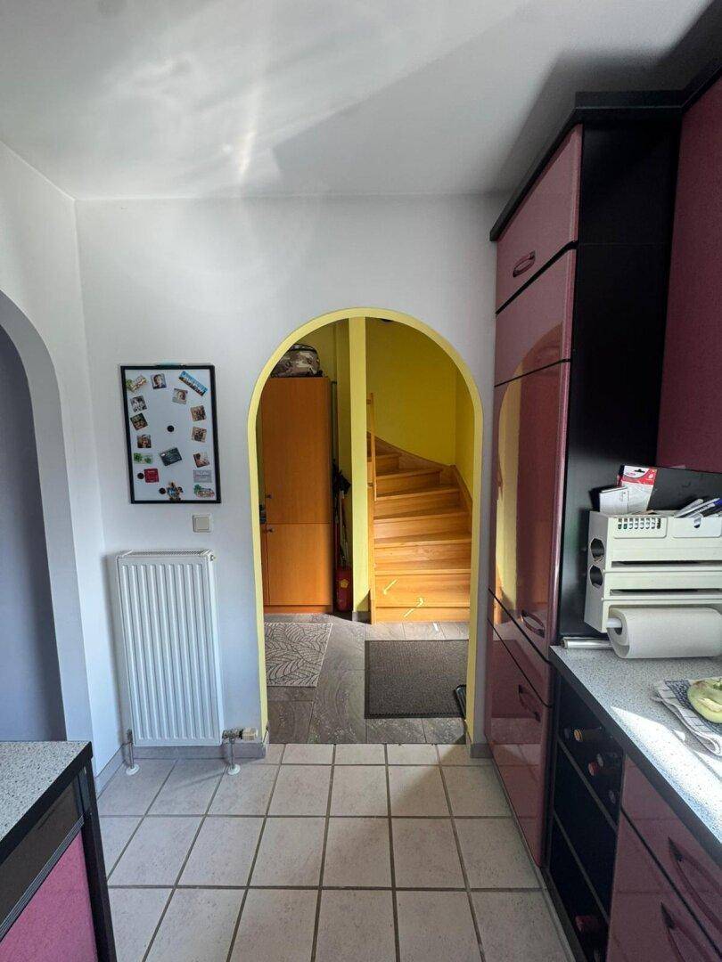 Küche mit rosa-schwarzen Schränken, Fliesenboden und einem Durchgang zum Treppenhaus.