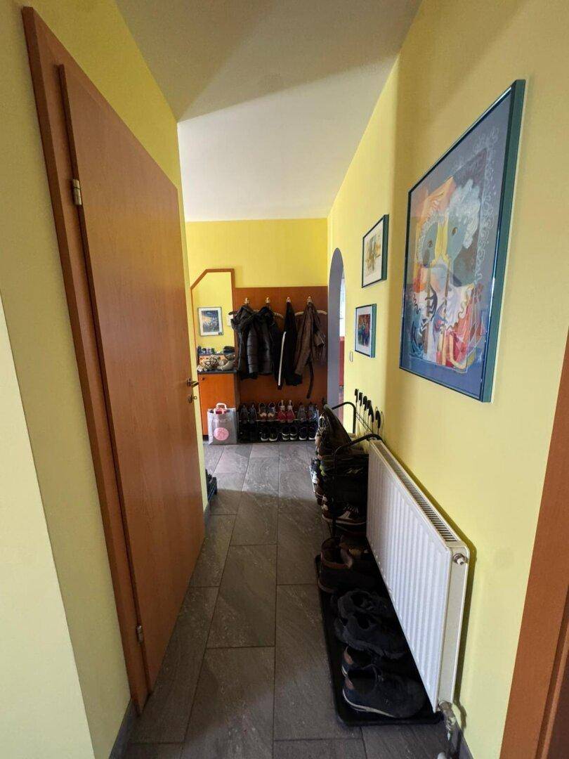Flur mit gelben Wänden, Schuhregal und Heizkörper, der zu weiteren Räumen führt.