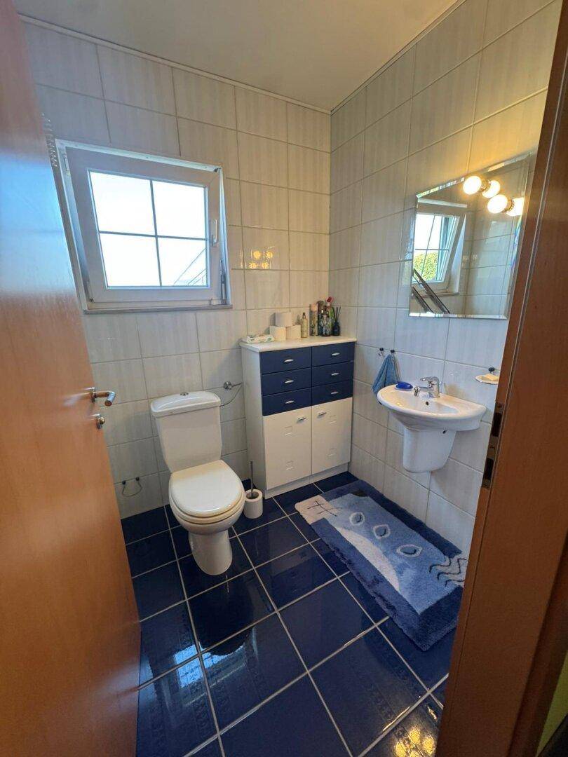 Kleines Badezimmer mit WC, Waschbecken, Fenster und blauen Bodenfliesen.
