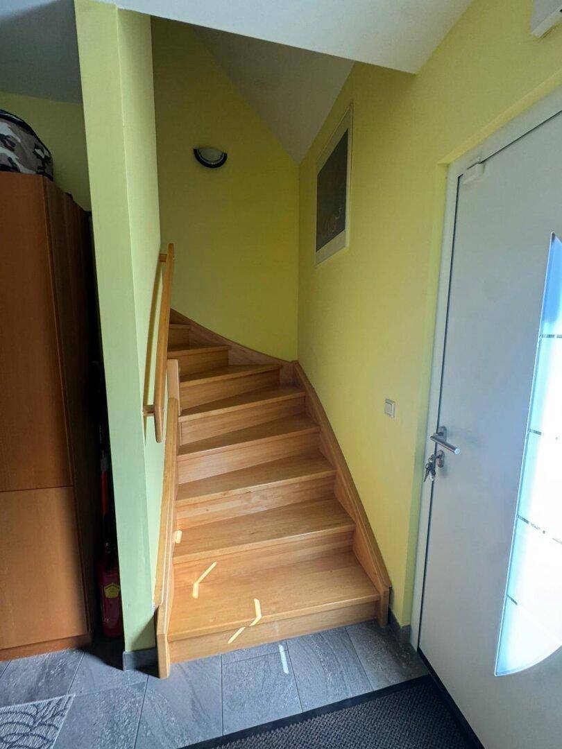 Holztreppe mit gelben Wänden, die in die oberen Stockwerke des Hauses führt.