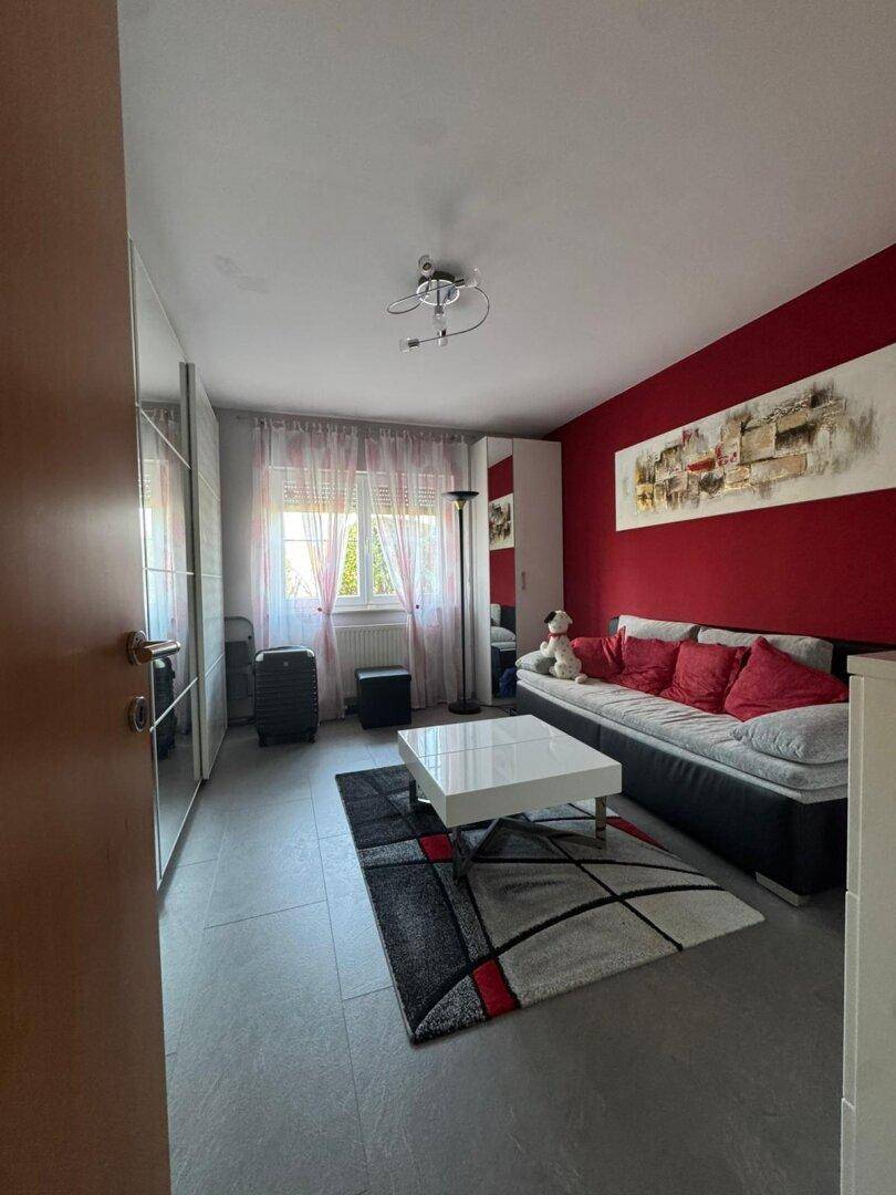 Wohnzimmer mit Schlafsofa, roter Akzentwand und großem Spiegelschrank, der den Raum optisch vergrößert.