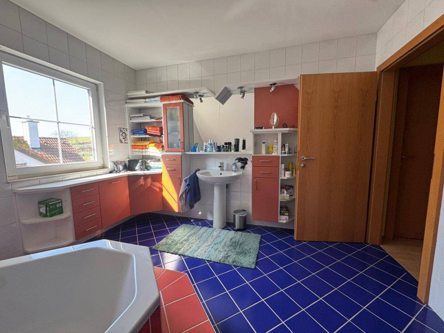 Dachgeschoss-Badezimmer mit Waschbecken, Schränken und einem Fenster, das den Raum erhellt.