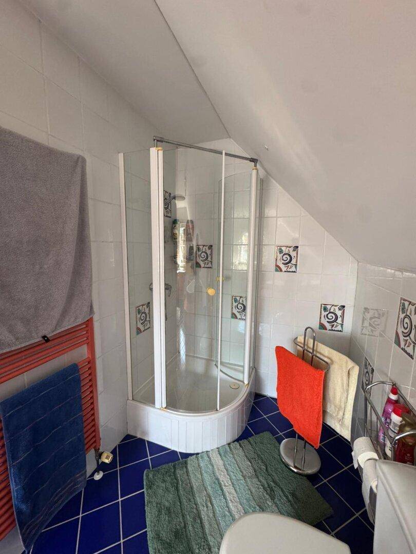 Dachgeschoss-Badezimmer mit Duschkabine und blauen Fliesen, unter einer charakteristischen Dachschräge.