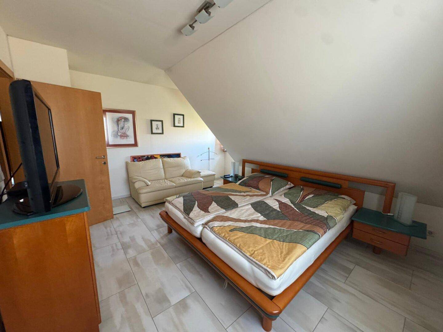 Dachgeschoss-Schlafzimmer mit Doppelbett, Sofa und Fenster, unter einer gemütlichen Dachschräge.