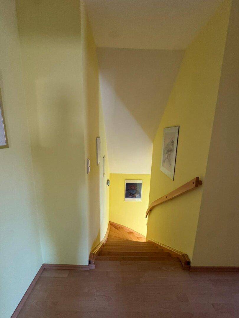 Treppenhaus mit gelben Wänden und Holzstufen, das in die unteren Etagen führt.