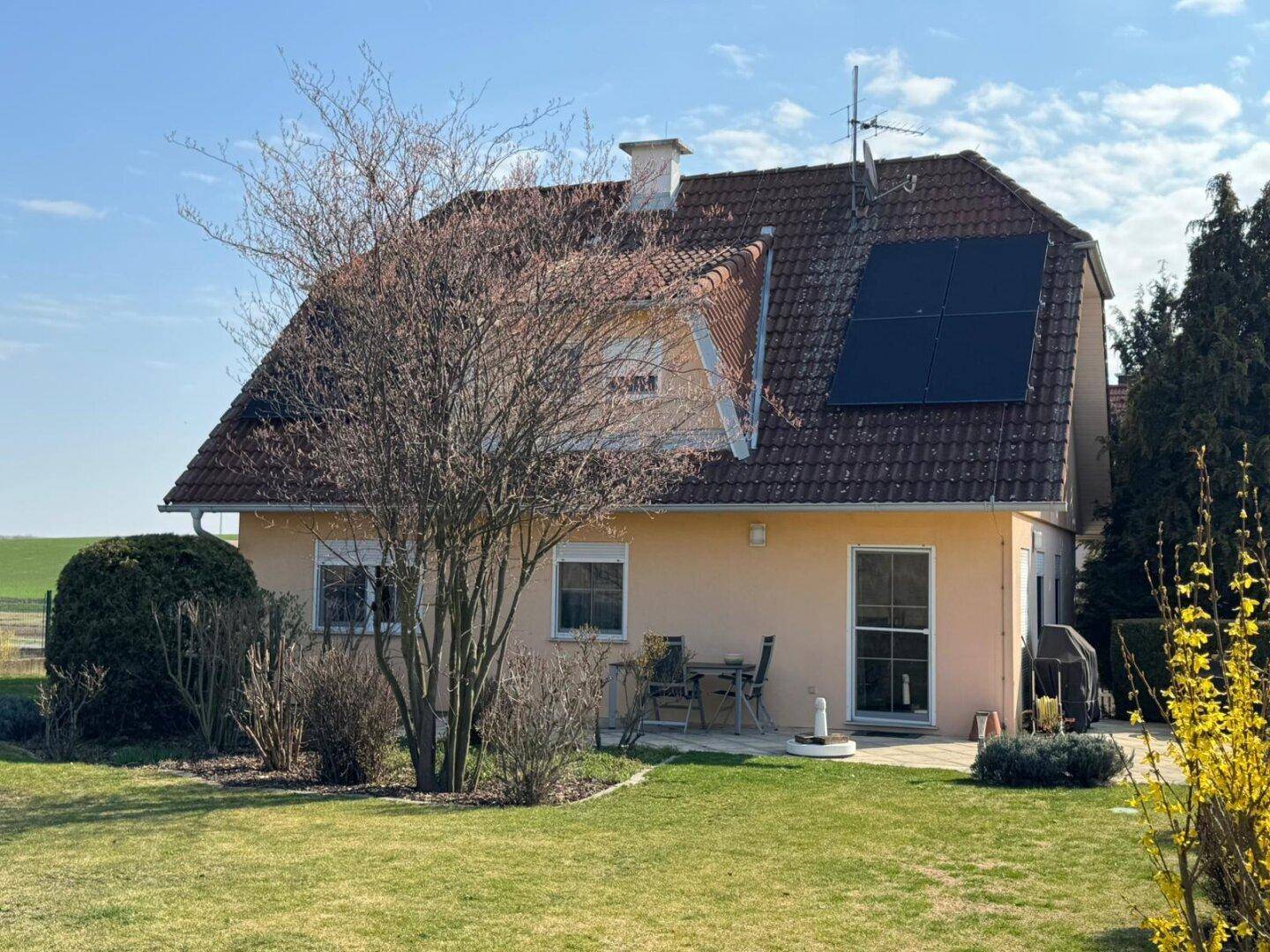 Rückansicht des Hauses mit gepflegtem Garten, kleiner Terrasse und Solaranlage auf dem Dach.