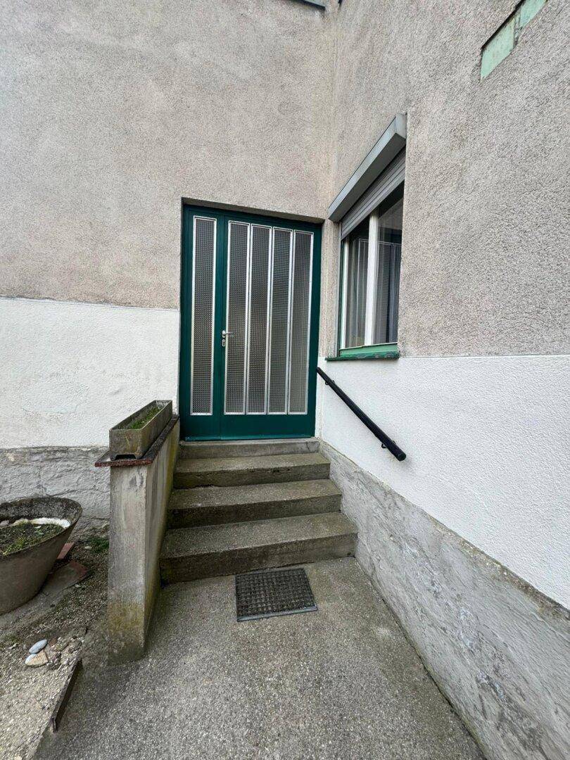 Nahaufnahme des Hauseingangs mit grüner Tür und kleiner Treppe.