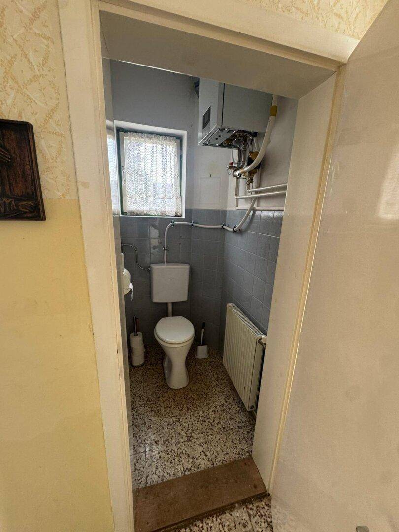 Kleines WC mit Fenster, Heizkörper und Wandfliesen in hellem Blau.