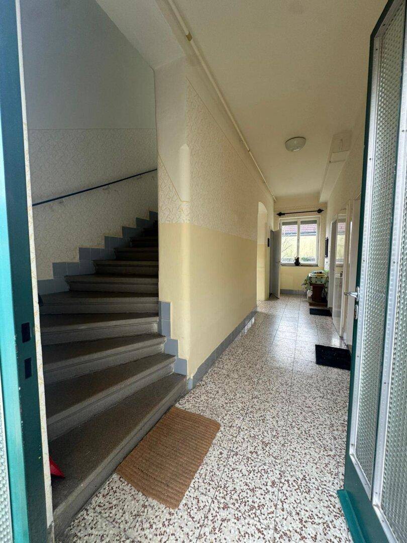 Heller Flur mit Terrazzoboden und Treppenaufgang in die oberen Stockwerke.