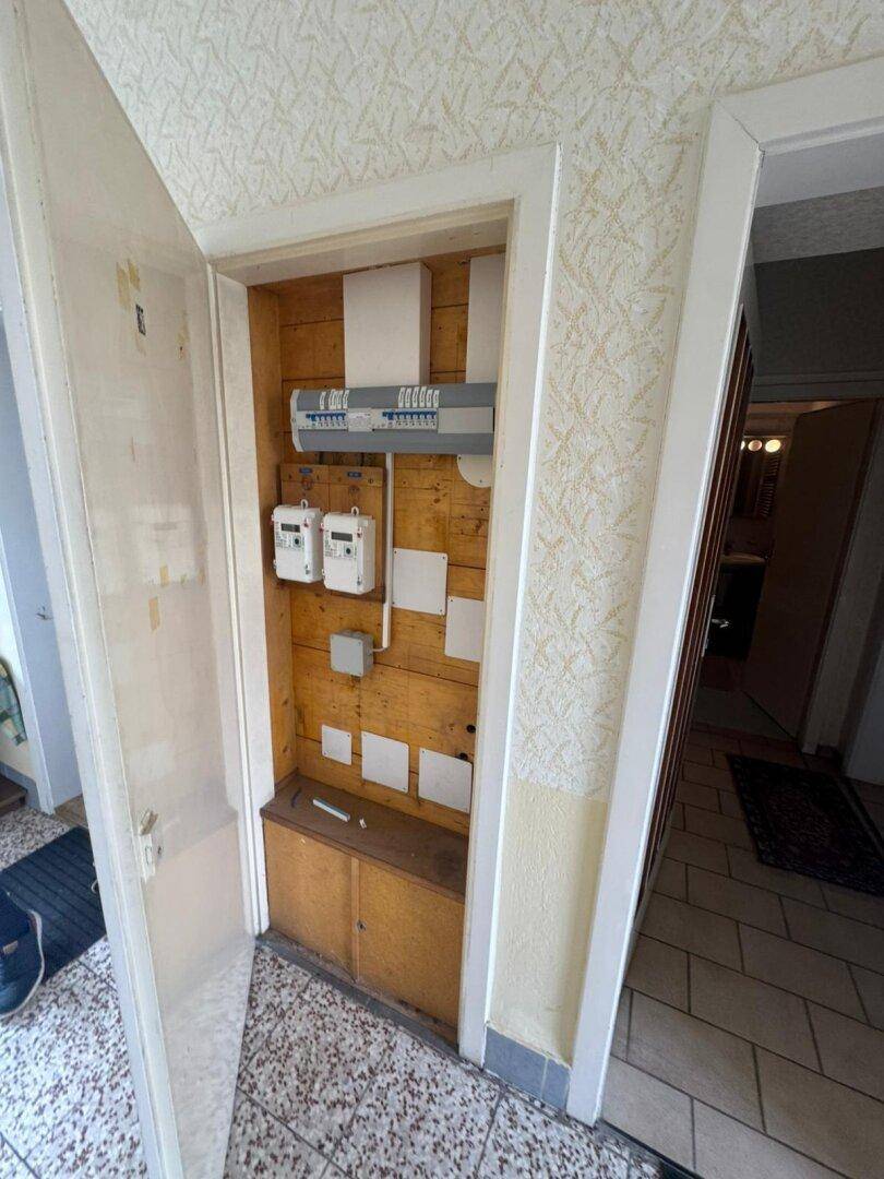 Offener Schrank mit Sicherungskasten und Zählern, in einem Holzregal integriert.
