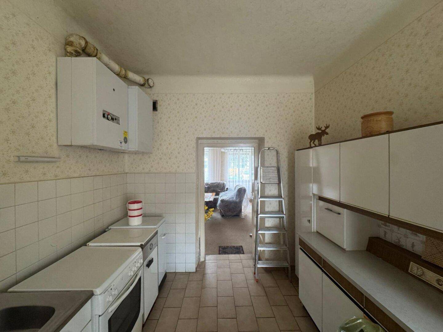 Küchenbereich mit Wandfliesen, Gastherme und Blick in einen angrenzenden Raum.