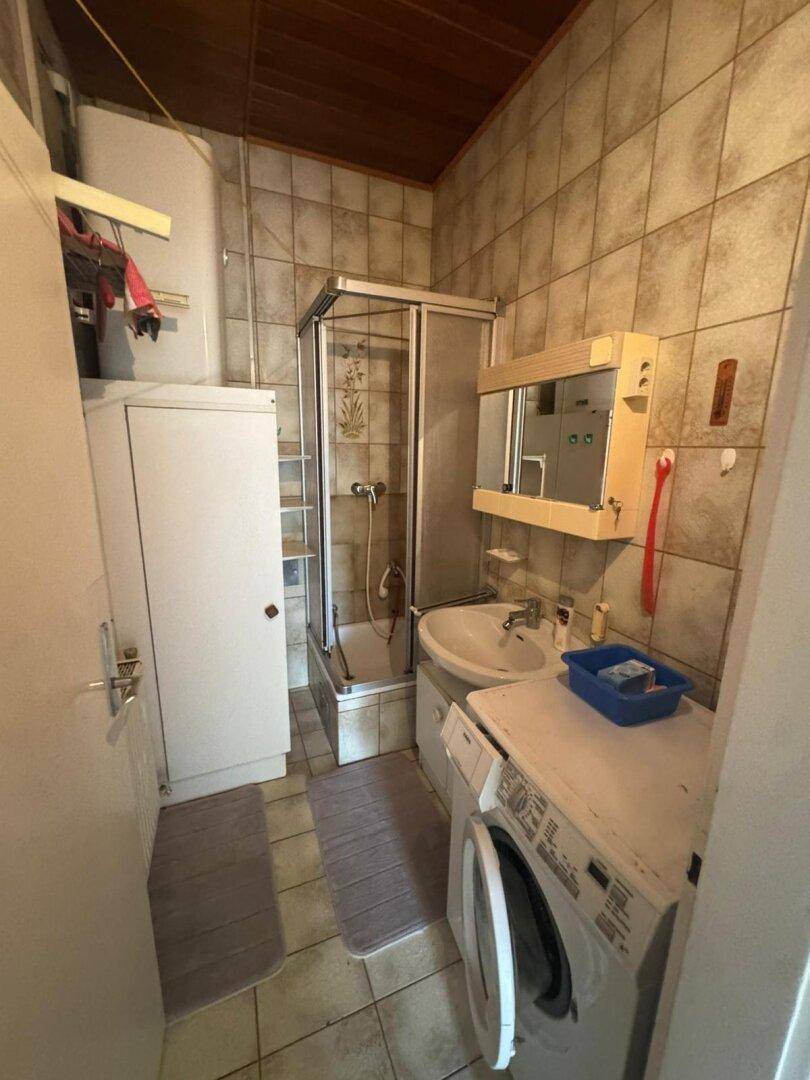 Badezimmer mit Duschkabine, Waschbecken und Wandfliesen in neutralen Tönen.