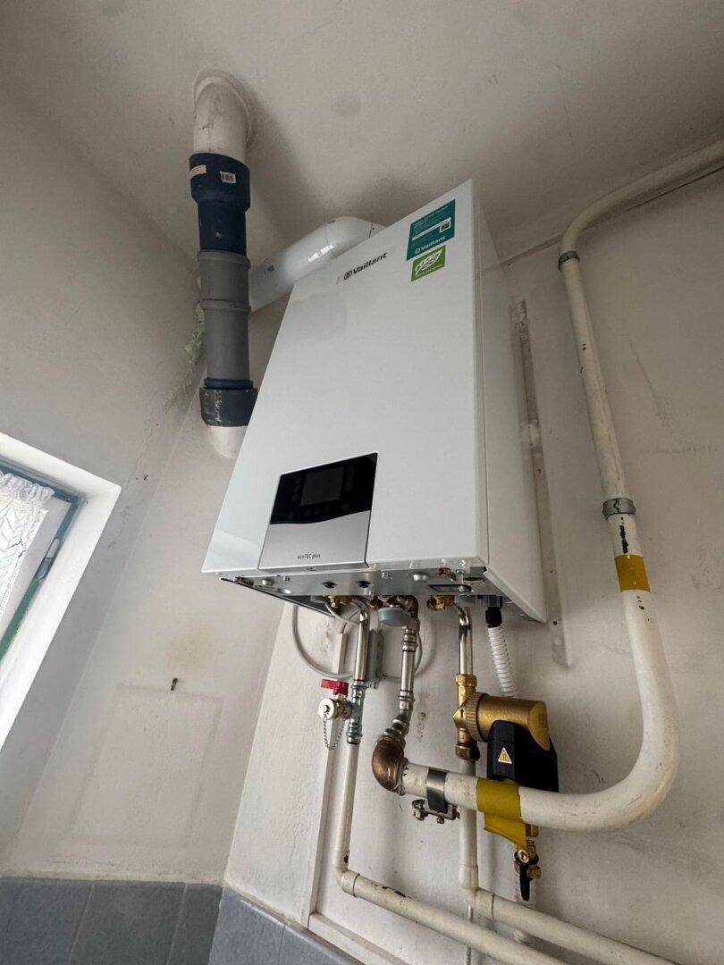 Moderne Gastherme an der Wand mit sichtbaren Rohren und Anschlüssen.