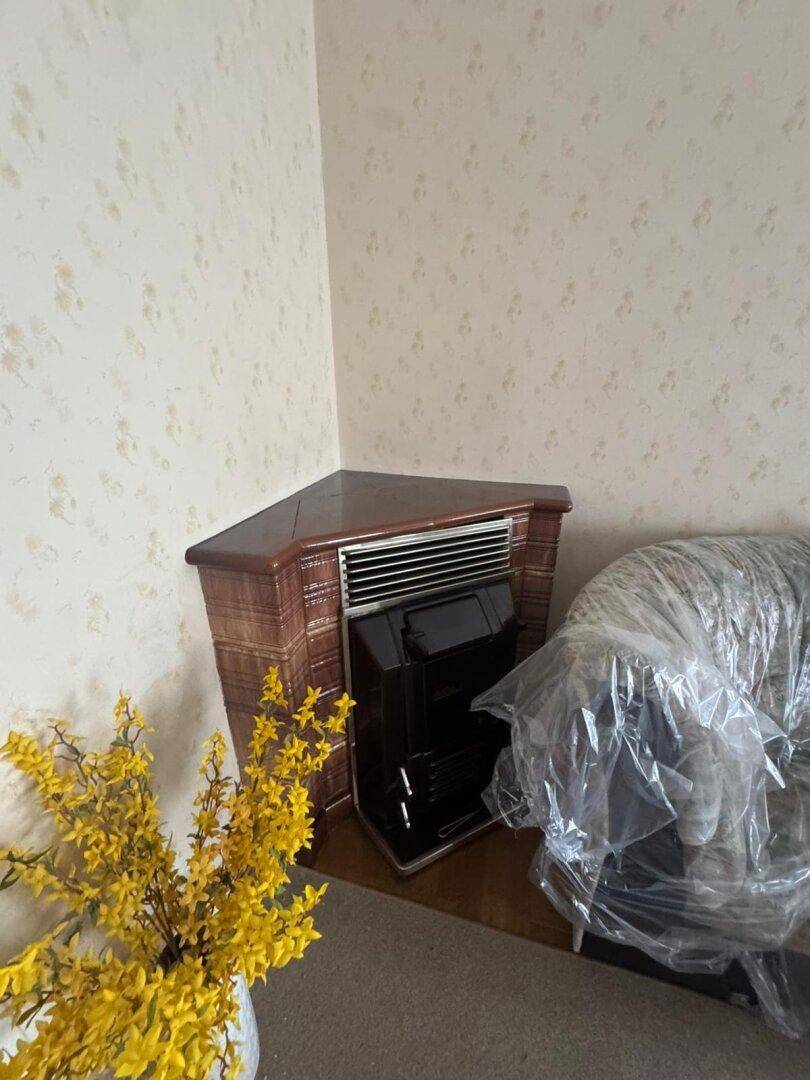 Eckheizofen im Wohnzimmer mit gemusterter Tapete und abgedeckten Möbeln.