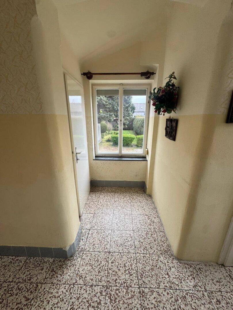 Eingangsbereich mit Terrazzoboden und Fenster zum Garten, bietet Zugang zu weiteren Räumen.