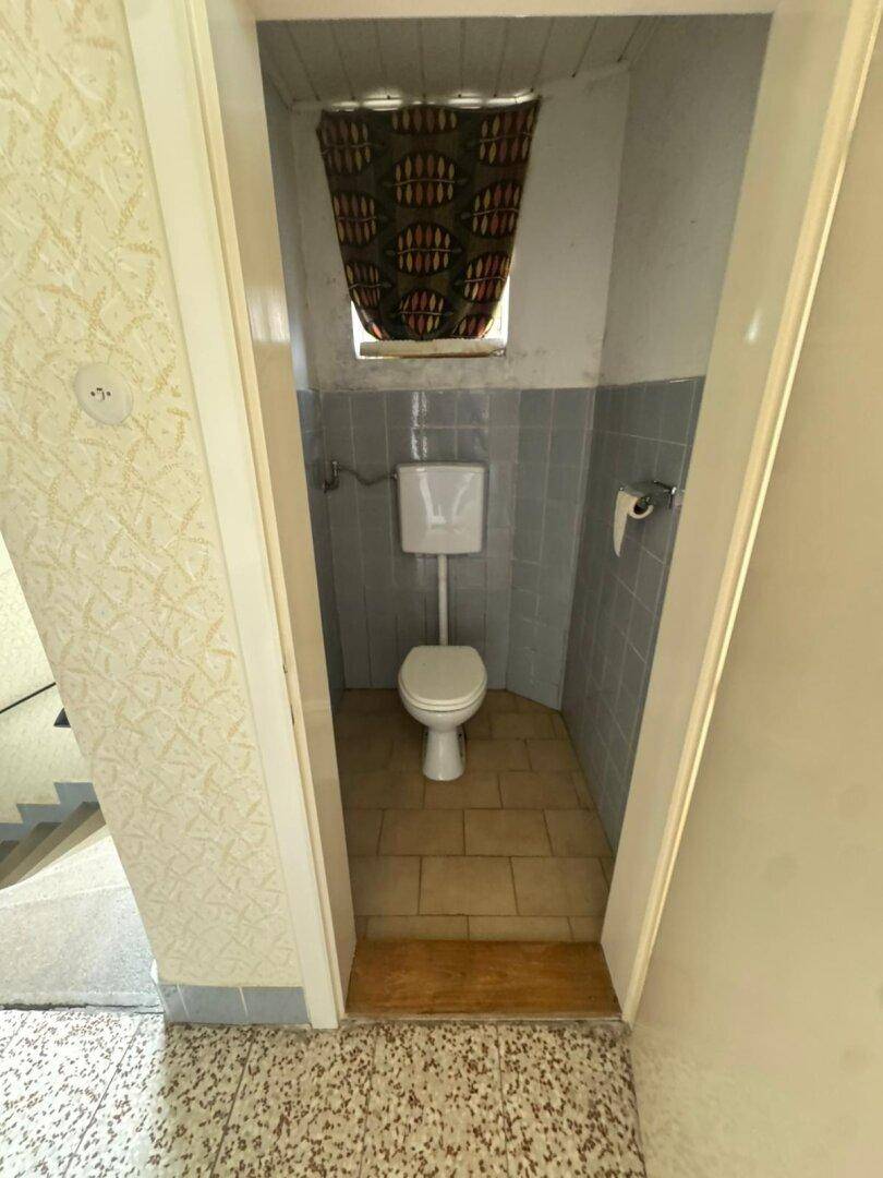 Kleines WC mit blauen Fliesen und Fenster, ausgestattet mit einer Standardtoilette.