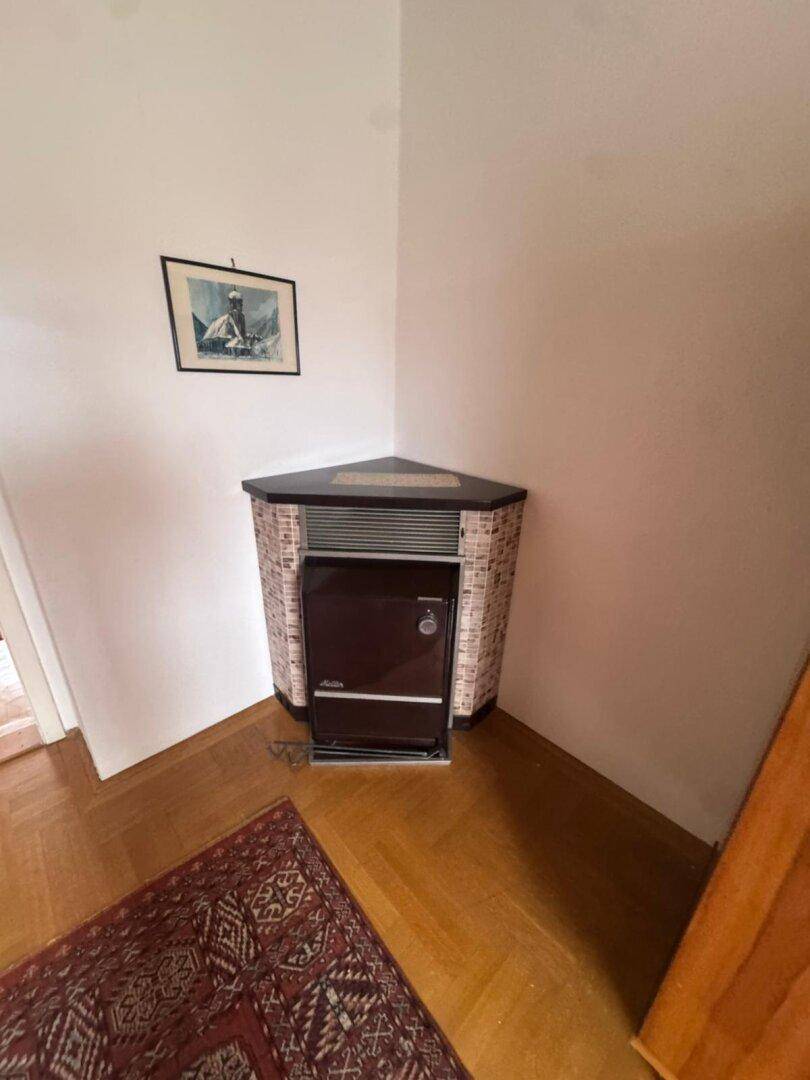 Eckheizofen in einem Zimmer mit Parkettboden und weiß gestrichenen Wänden.
