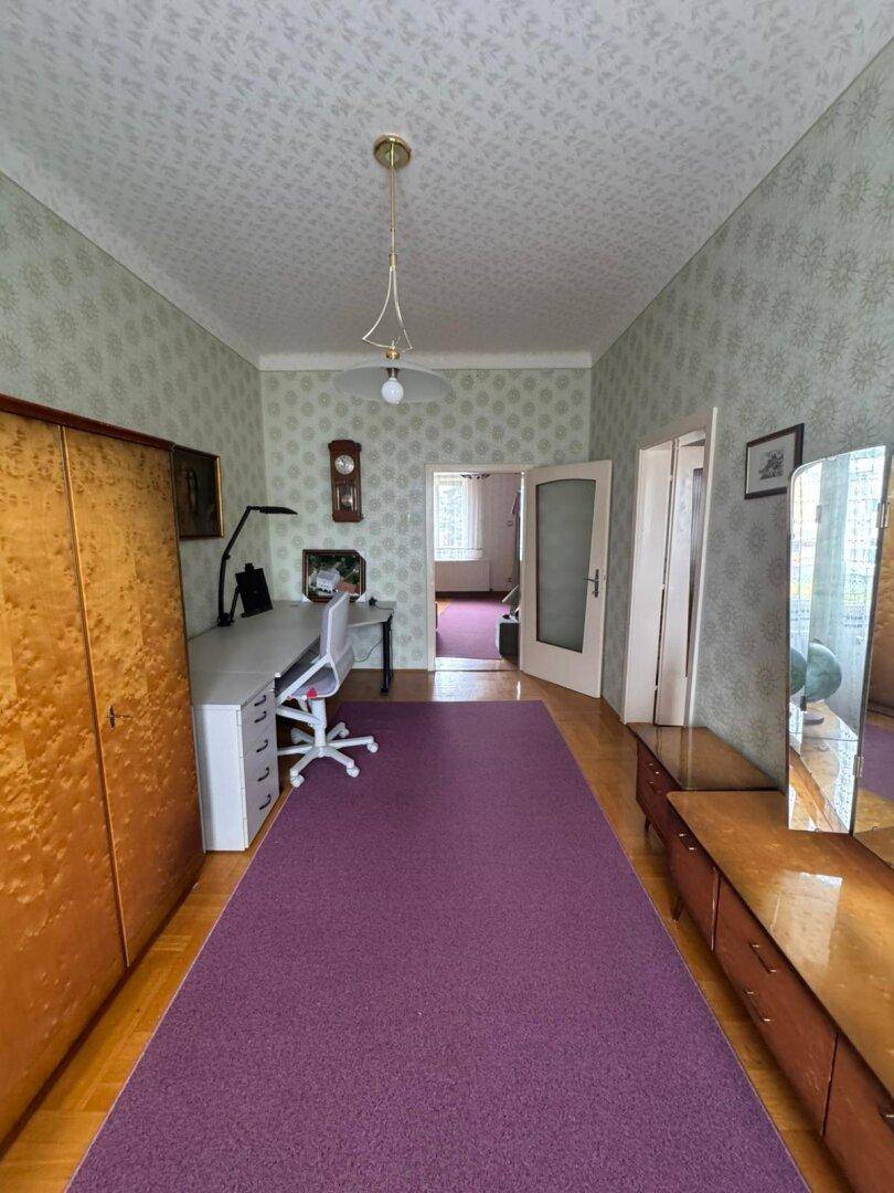Schlafzimmer mit lila Teppichläufer, Parkettboden und einem Schreibtischbereich.