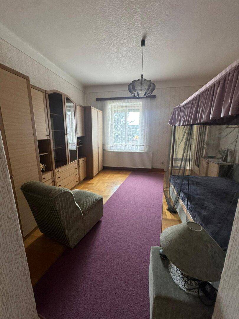 Schlafzimmer mit Himmelbett, lila Teppichläufer und Holzschränken.