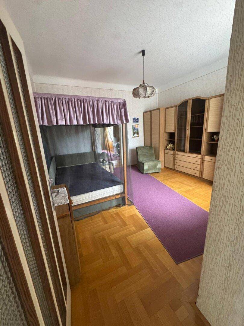 Schlafzimmer mit Himmelbett, lila Teppichläufer und Holzschränken, Blick vom Eingang.