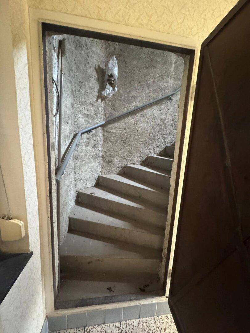 Schmaler Treppenabgang mit Betonstufen und Metallgeländer führt in einen Kellerbereich.