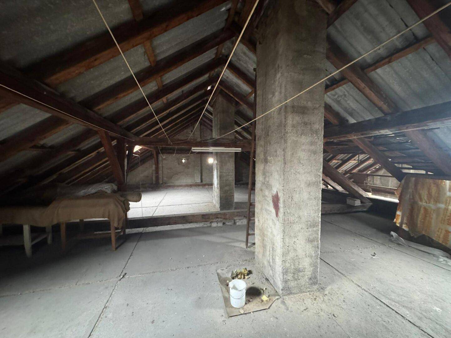 Großer Dachboden mit freiliegenden Holzbalken, Betonboden und einem massiven Kaminzug.