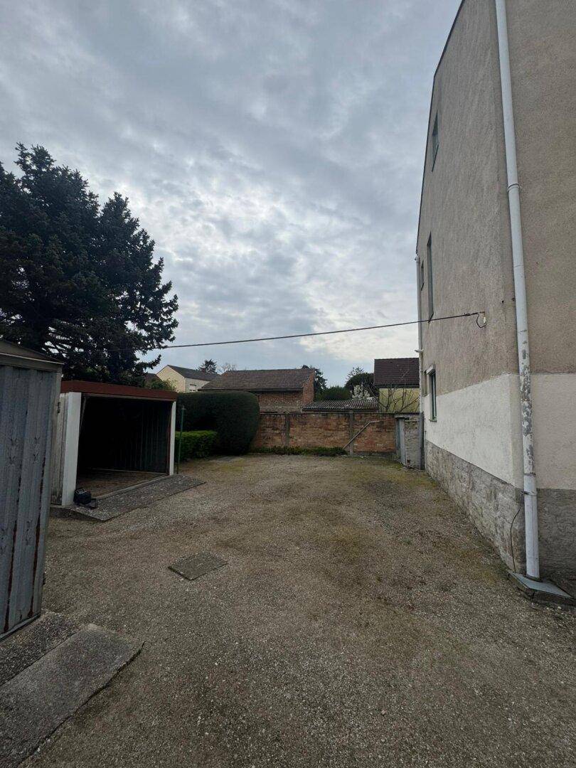 Großer Schotterplatz neben einem Gebäude mit einem einfachen Carport und viel Freifläche.