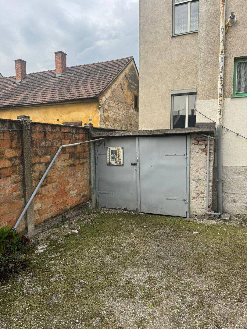 Metalltor in einer Ziegelmauer führt zu einem kleinen gepflasterten Bereich neben dem Gebäude.