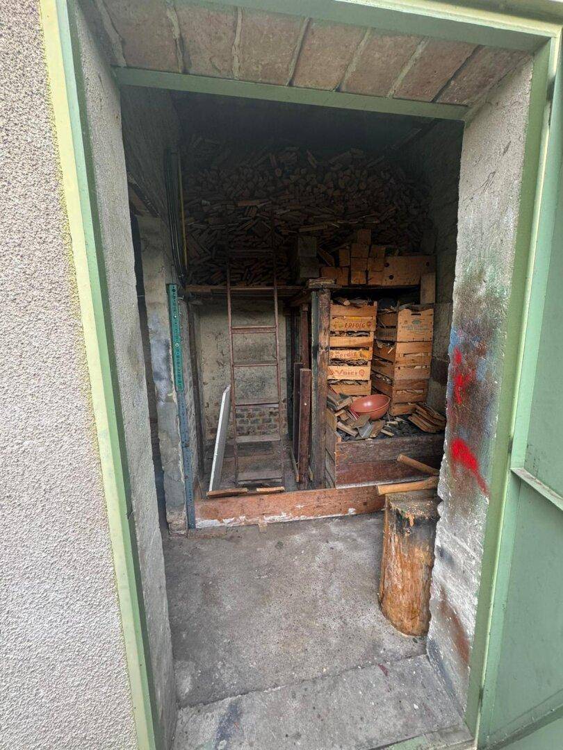 Lagerraum gefüllt mit Brennholz und Kisten, eine Leiter steht bereit.