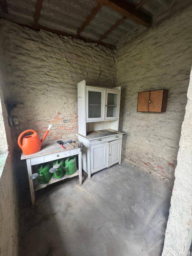 Einfacher Wirtschaftsraum mit altem Schrank, Tisch und Gartengeräten.
