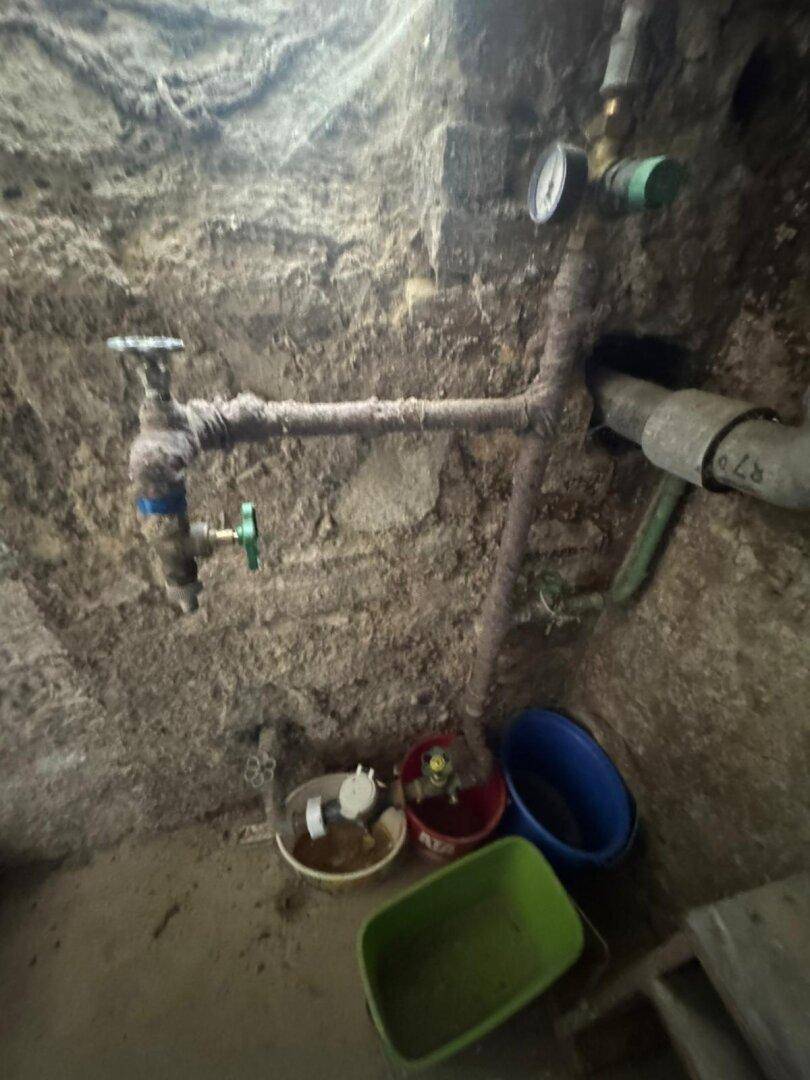 Detailaufnahme von alten, rostigen Wasserleitungen und Ventilen in einem unfertigen Raum.