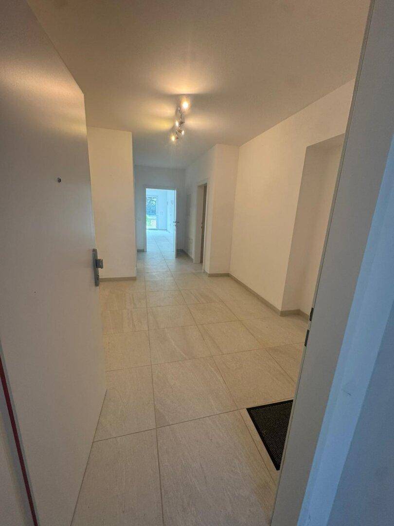 Renovierter Flur mit hellen Fliesen, modernen Deckenleuchten und weiß gestrichenen Wänden.